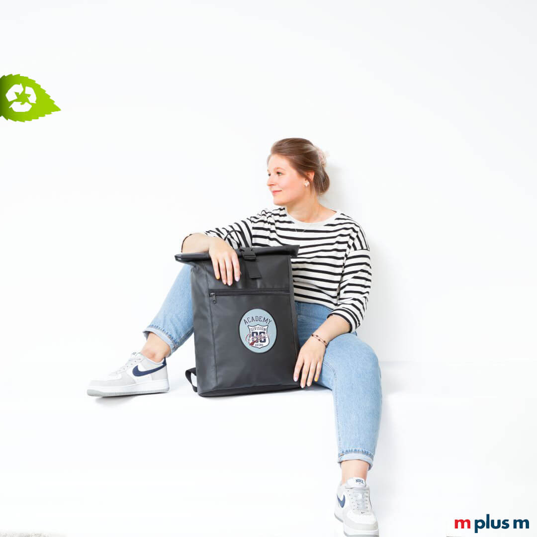 Frau sitzt entspannt mit schwarzem Kurrier Economy Rucksack aus LKW-Plane mit Logo, modischer und nachhaltiger Alltagsbegleiter.